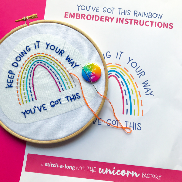 An almost finished rainbow embroidery project in a hoop on top of the instructions for the project